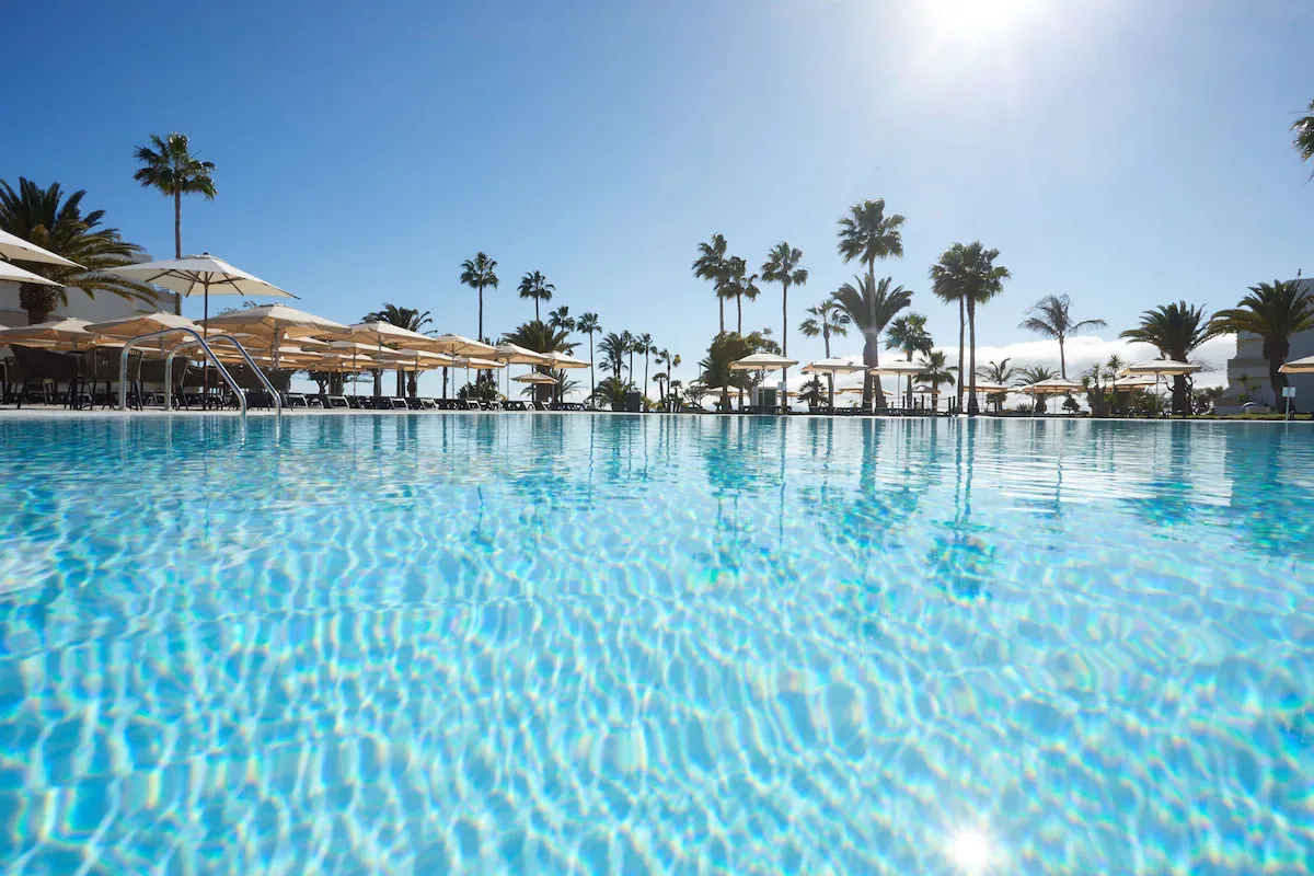 Large pool lined with palm trees and parasols at Grand Hyatt Lanzarote Playa Dorada