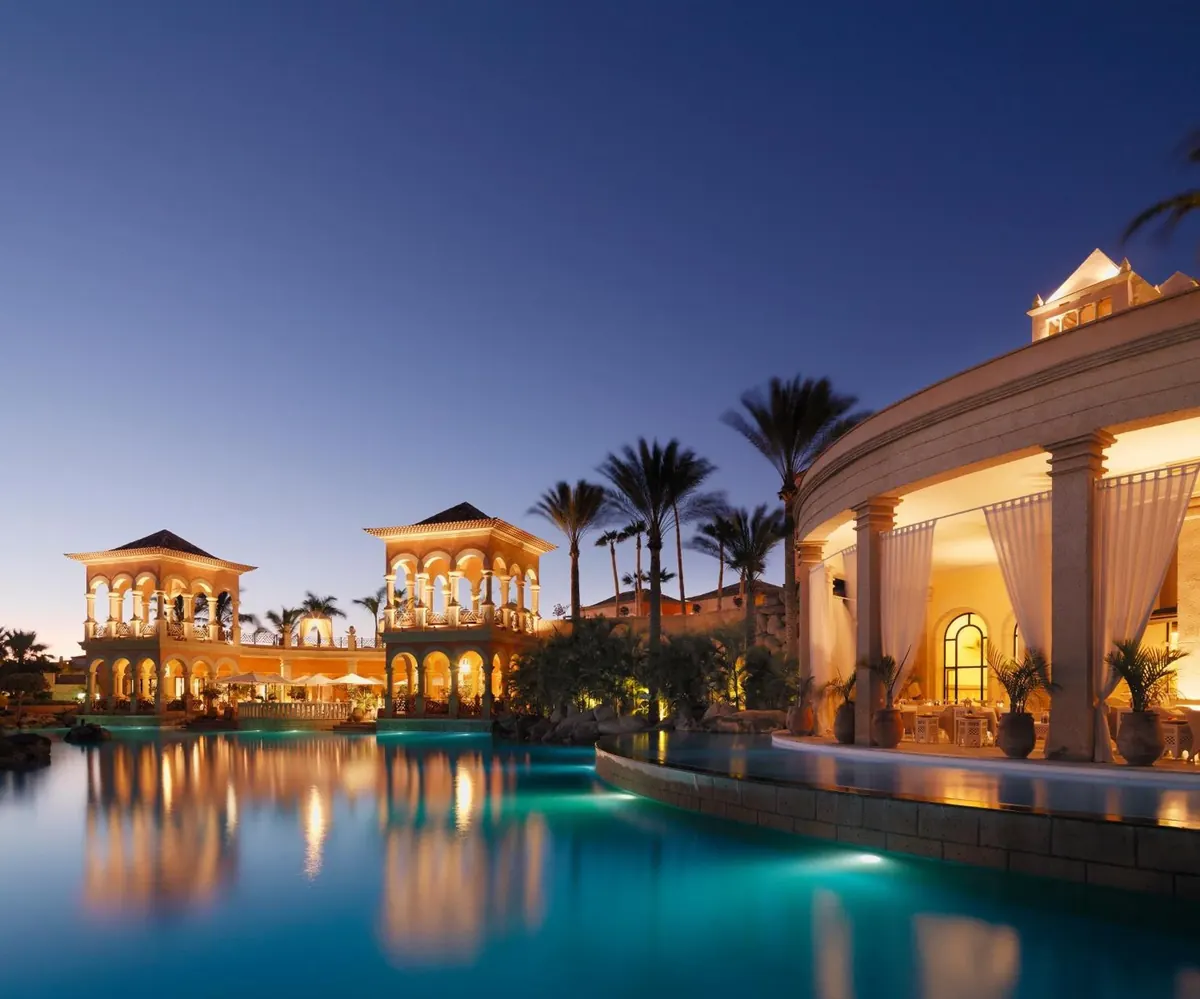 Illuminated arched pavilions reflected in the pool at dusk at JOIA El Mirador by Iberostar, Costa Adeje