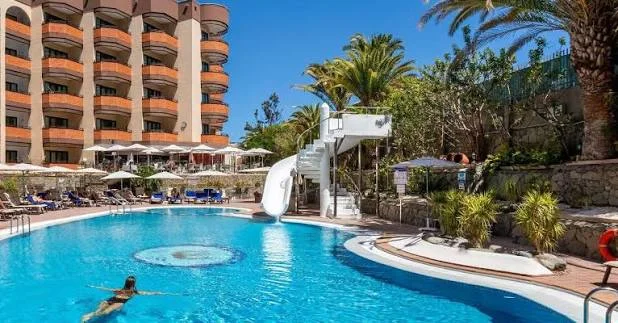 Pool with water slide beside the orange-toned facade of MUR Hotel Neptuno Gran Canaria in Playa del Inglés