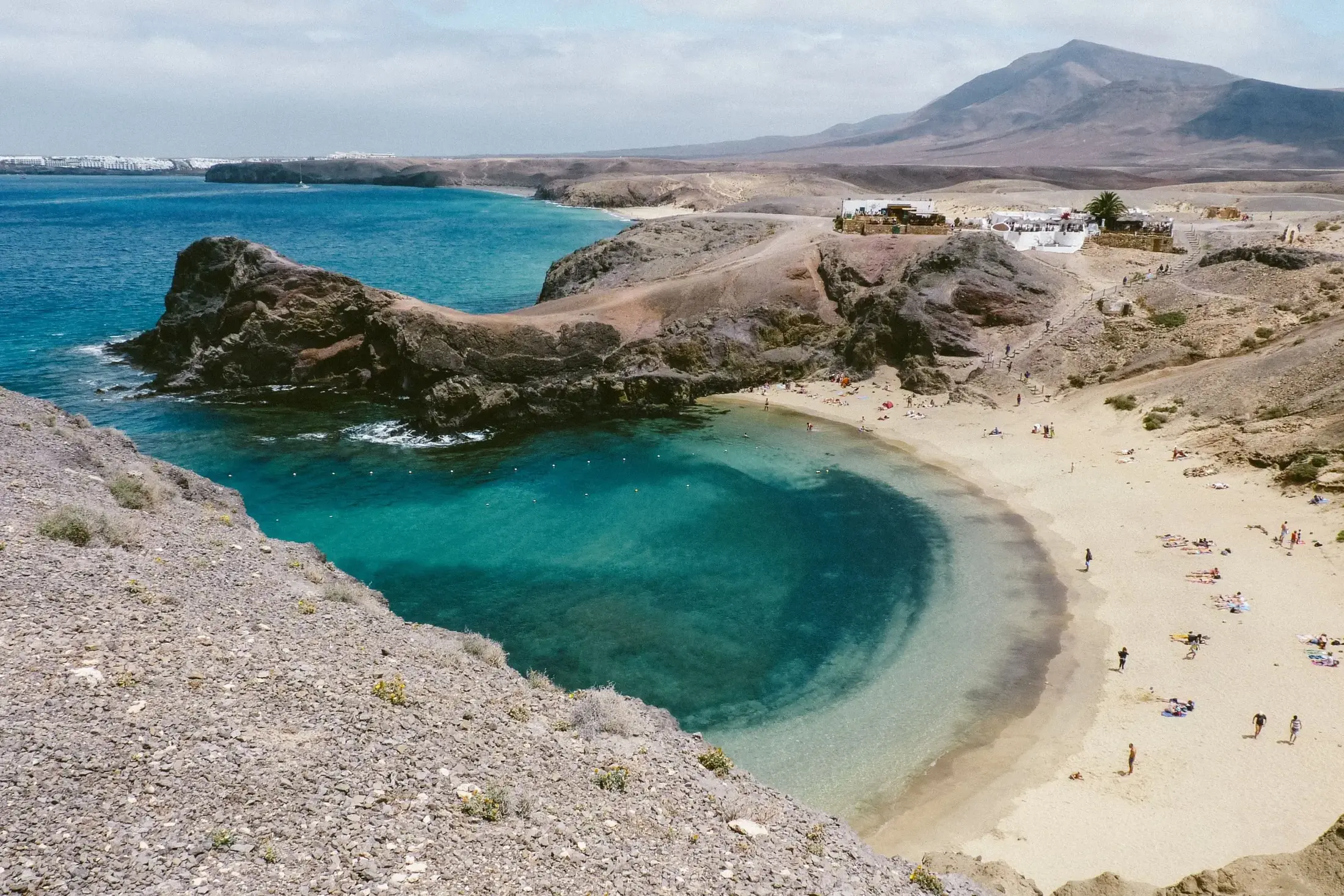 Playa de Papagayo from the clifftop, with the restaurants above the cove and the Los Ajaches hills behind
