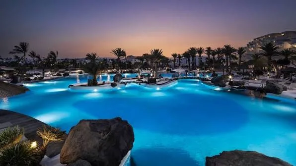 Illuminated saltwater lagoon pool at dusk surrounded by palm trees at Paradisus Salinas Lanzarote in Costa Teguise