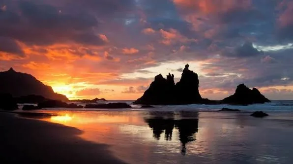Sunset over the sea stacks of the Roques de Anaga from the black sand of Playa de Benijo