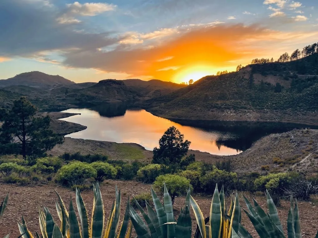 Sunset reflected in the Presa de las Niñas reservoir, surrounded by pine-covered hills