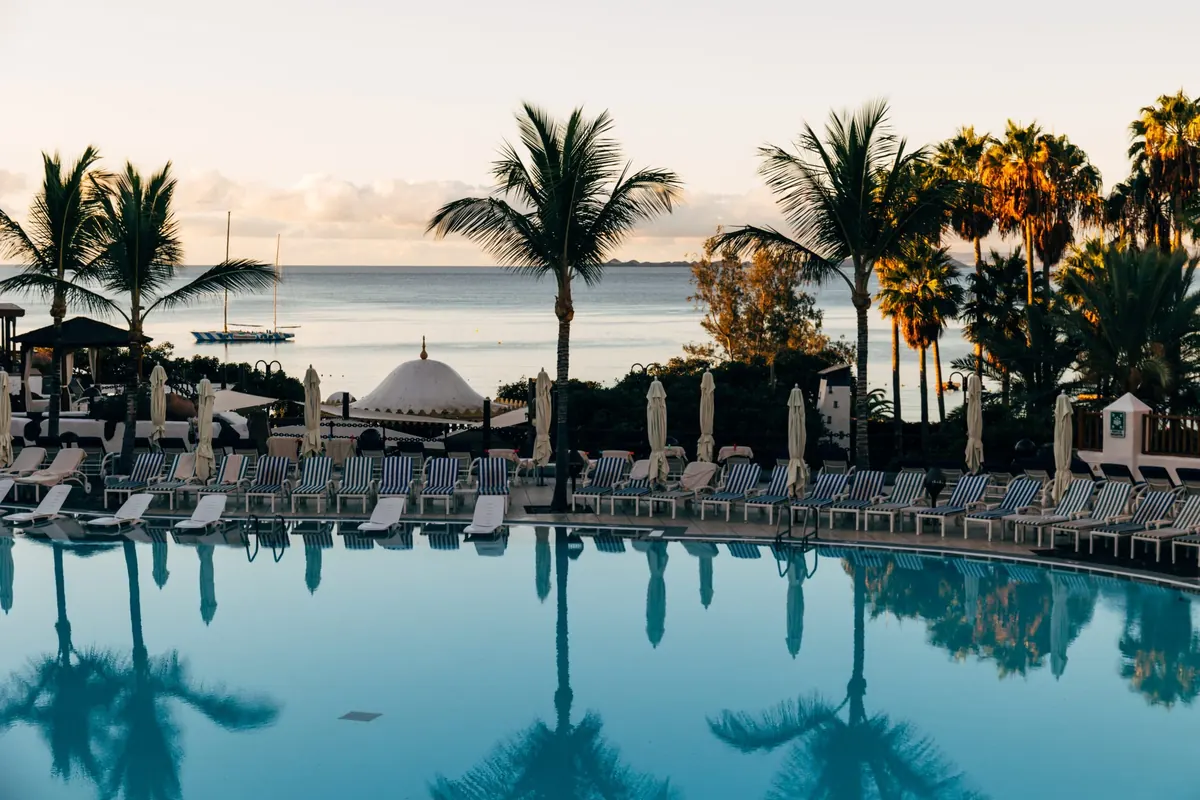 Pool framed by palm trees at sunrise overlooking the sea at Princesa Yaiza Suite Hotel Resort, Playa Blanca