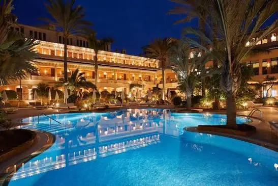 Illuminated pool terrace at night surrounded by palm trees at Secrets Bahía Real Resort & Spa in Corralejo, Fuerteventura