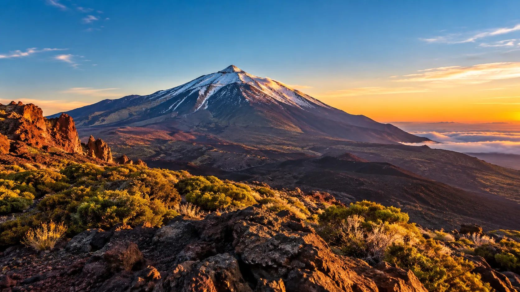 Snow-capped Mount Teide at sunrise above a sea of clouds, seen from the rocky rim of Las Cañadas